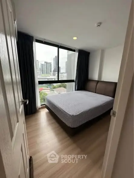 Modern bedroom with large window and city view, featuring a comfortable bed and stylish decor.