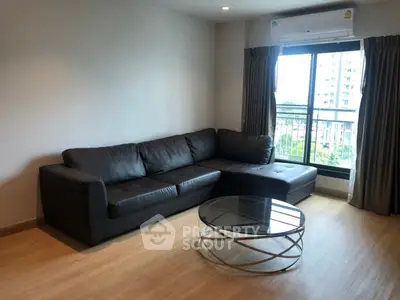 Modern living room with sleek black sofa and glass coffee table, featuring a large window with city view.