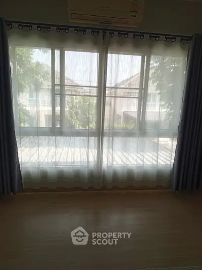 Bright living room with large windows and sheer curtains offering a serene view of the outdoors.