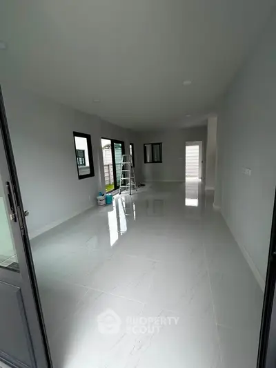 Spacious modern living room with glossy white tiles and large windows, perfect for natural light.