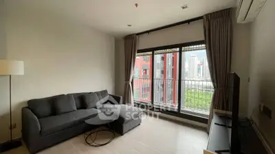 Modern living room with city view, featuring a sleek gray sofa and large windows.