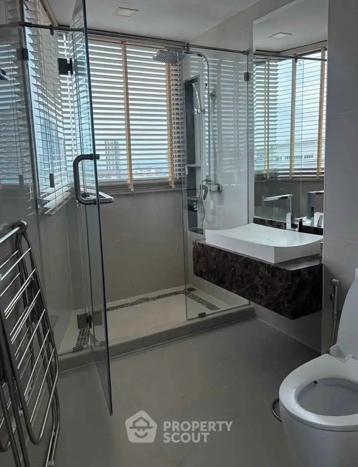 Modern bathroom with glass shower, sleek fixtures, and city view through large windows.