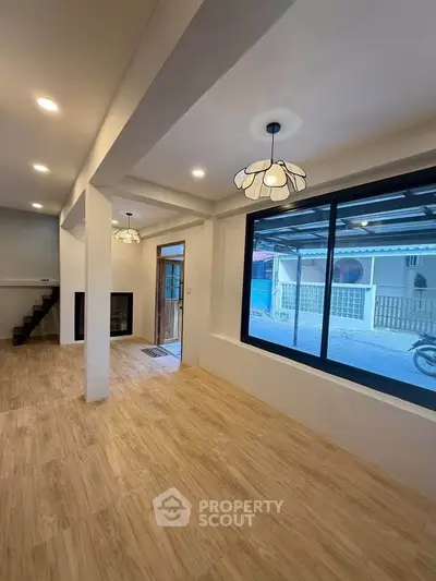 Spacious modern living room with large window and stylish lighting, showcasing open layout and wooden flooring.