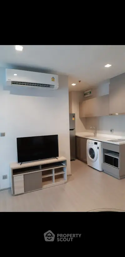 Modern apartment interior with compact kitchen and living area featuring TV, washing machine, and air conditioning.