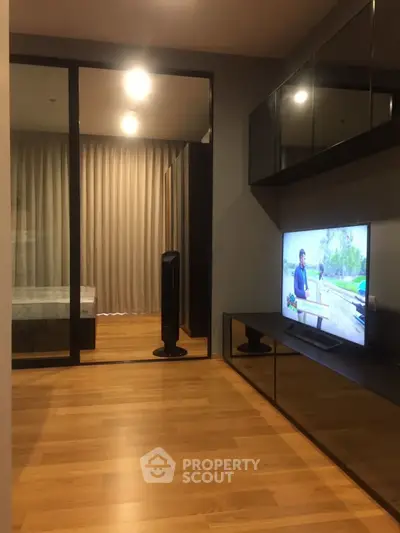 Modern living room with sleek wooden flooring and a wall-mounted TV, adjacent to a cozy bedroom.