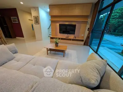 Spacious modern living room with plush sofa and large TV, overlooking a serene outdoor view.