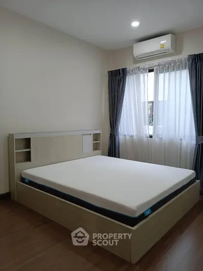 Modern bedroom with wooden flooring, stylish bed, and natural light from window.