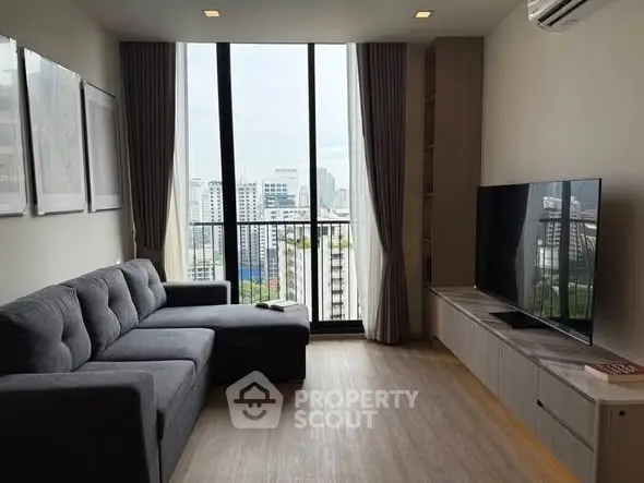 Modern living room with large windows and city view, featuring a stylish gray sofa and sleek entertainment unit.