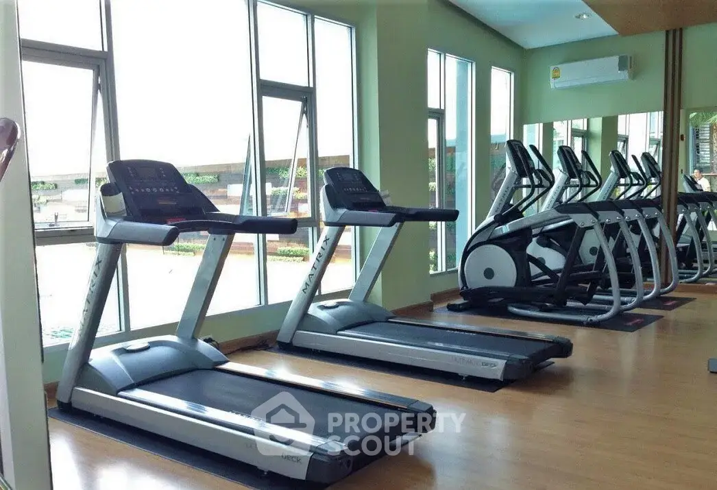 Modern gym with treadmills and elliptical machines in a bright, spacious room with large windows.