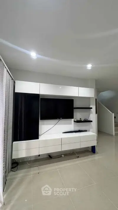 Modern living room with sleek white entertainment unit and flat-screen TV, showcasing minimalist design.
