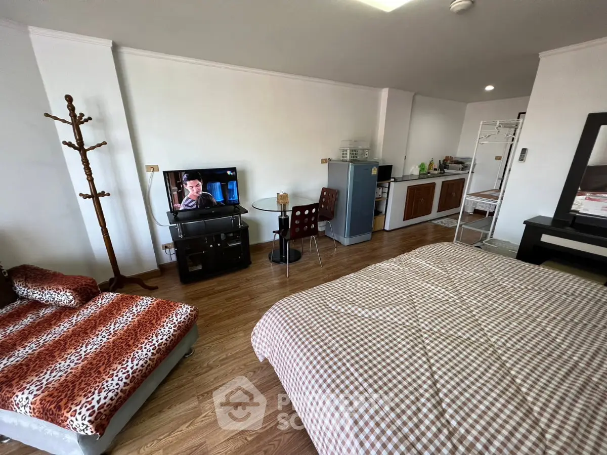 Spacious studio apartment with modern furnishings and open layout, featuring a cozy bed, TV, and kitchenette.