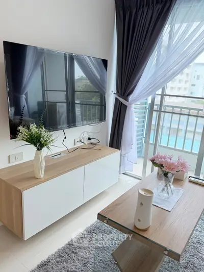 Modern living room with sleek TV setup and balcony view, featuring elegant decor and natural light.