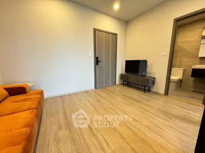 Modern living room with wooden flooring, orange sofa, and TV unit, adjacent to a sleek bathroom.
