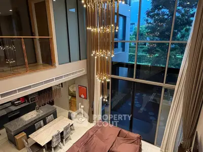 Luxurious modern living room with high ceilings and stunning chandelier, featuring floor-to-ceiling windows and elegant decor.