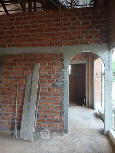 Under-construction brick wall interior with archway and construction materials.