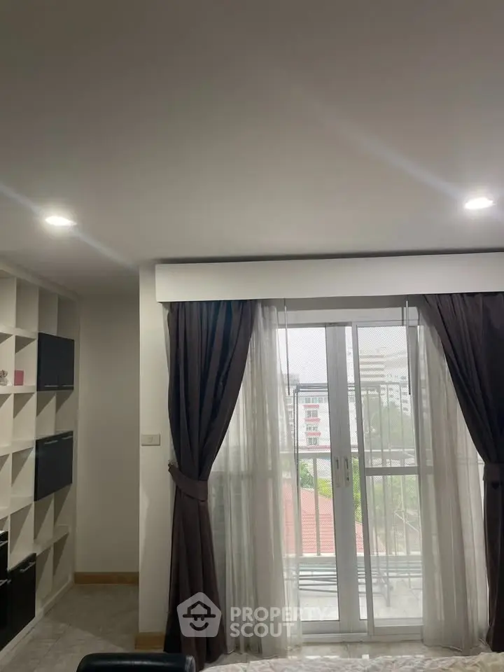 Modern apartment with large window and city view, featuring elegant curtains and built-in shelving.