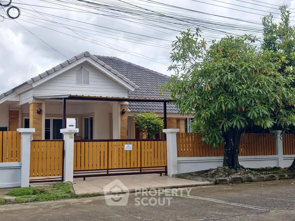 Charming single-story house with a tiled roof, fenced yard, and lush tree, perfect for family living.