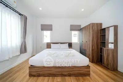 Modern bedroom with wooden flooring and stylish furniture, featuring a cozy bed and ample natural light.