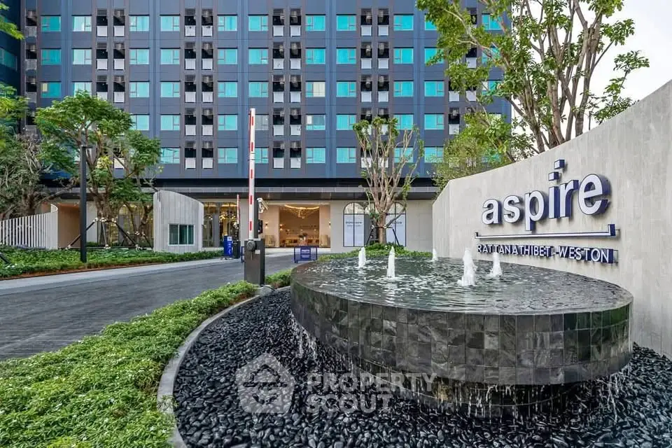 Modern apartment building entrance with stylish water feature and lush landscaping.