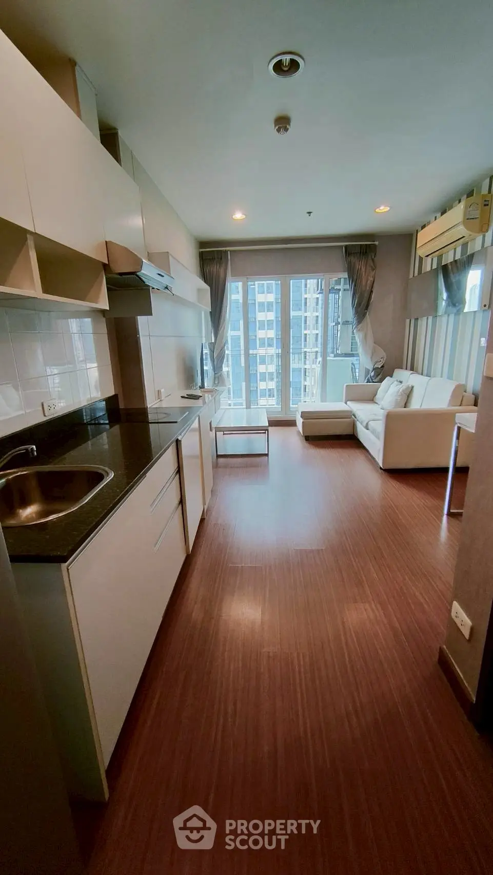 Modern living room with open kitchen and city view, featuring sleek white cabinetry and cozy seating area.