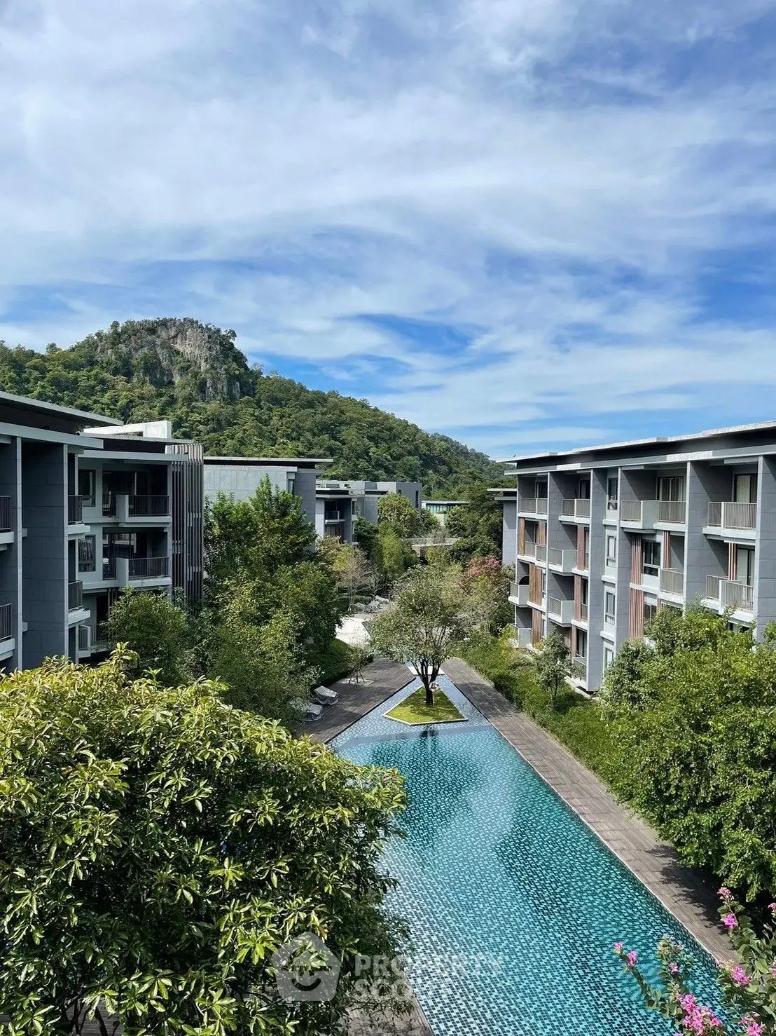 Luxurious resort-style condominium complex with a stunning infinity pool, lush greenery, and a majestic mountain backdrop, offering a serene living experience.
