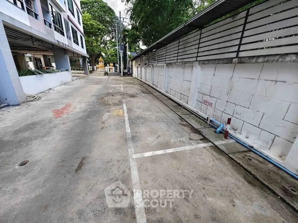 Spacious parking area beside modern building with secure fencing and lush greenery.
