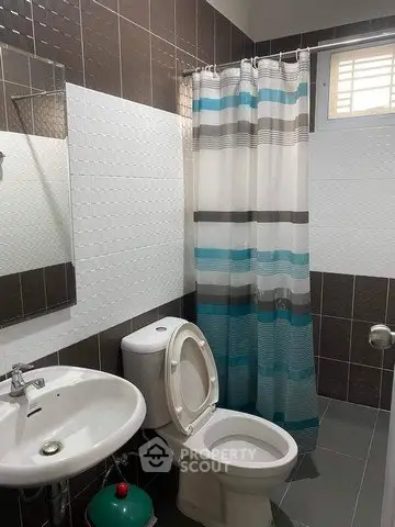 Modern bathroom with stylish tiles and shower curtain, featuring a sleek sink and toilet.