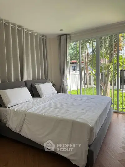 Spacious bedroom with large windows overlooking a lush garden, featuring elegant curtains and a cozy bed.