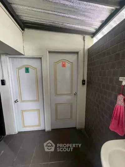 Compact bathroom area with two doors and a sink, featuring a tiled wall and ceiling light.