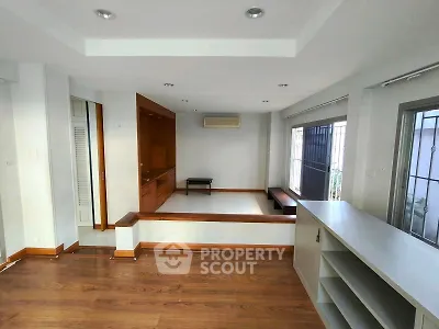 Spacious living room with wooden flooring and built-in shelves, featuring large windows for natural light.
