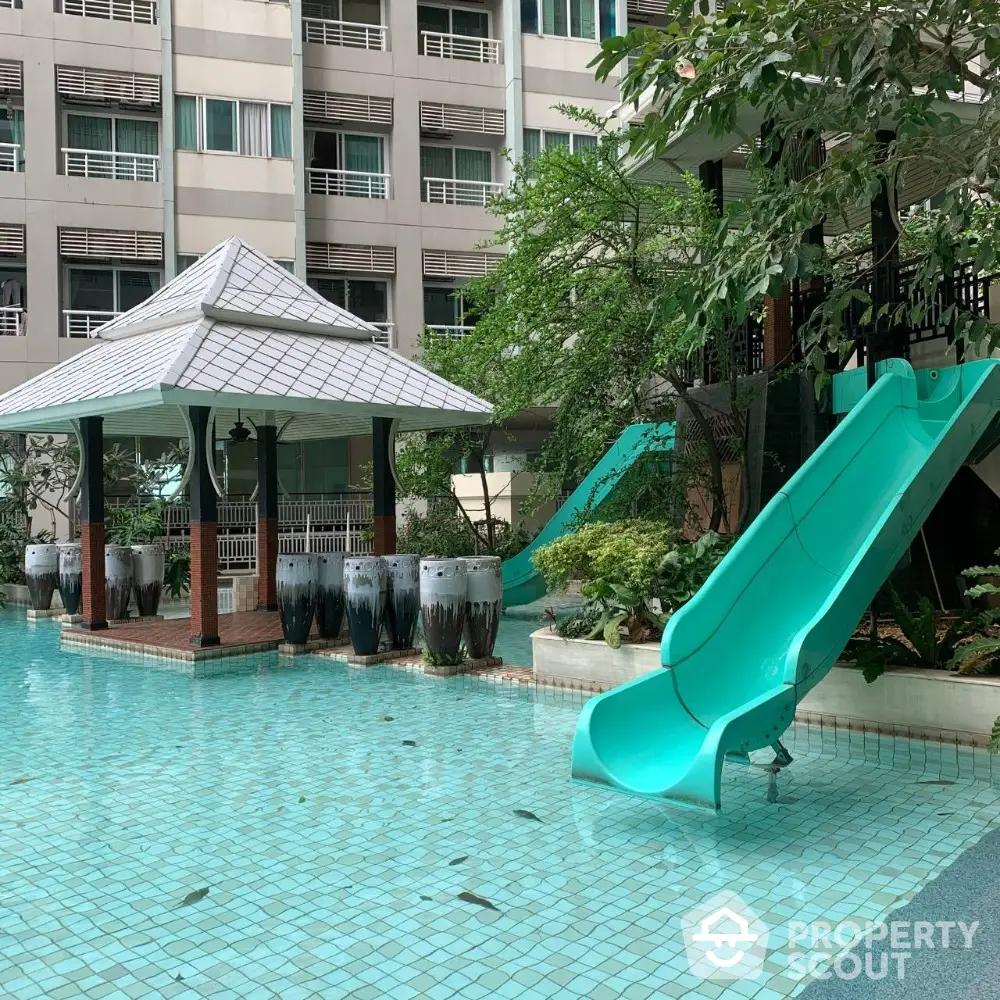 Luxurious condominium pool area with slide and lush greenery