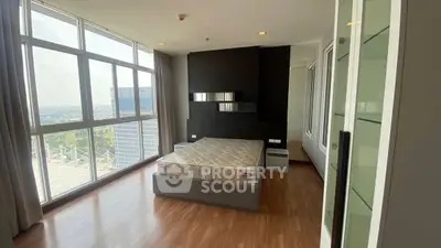 Spacious bedroom with large windows offering stunning city views and modern decor.