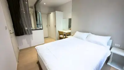 Modern bedroom with white bedding, wooden flooring, and a small study area, perfect for cozy living.