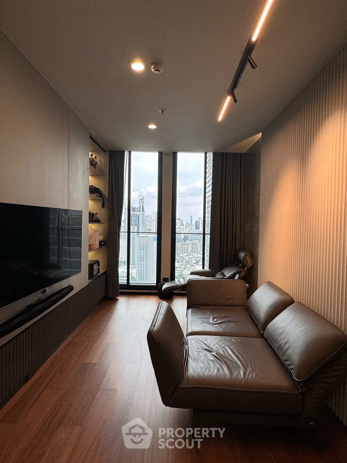 Modern living room with sleek design and stunning city view, featuring leather sofa and large TV.
