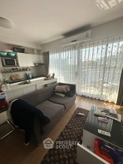 Cozy living room with open kitchen and balcony view, featuring modern appliances and natural light.
