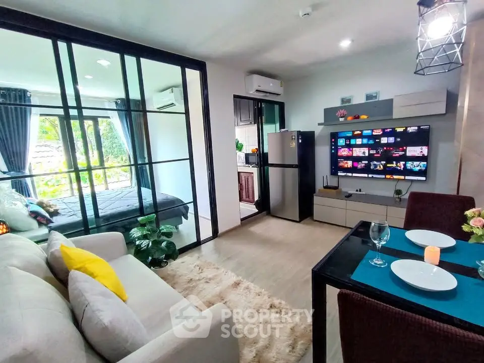 Modern open-plan living room with cozy decor and smart TV, adjacent to a glass-walled bedroom.