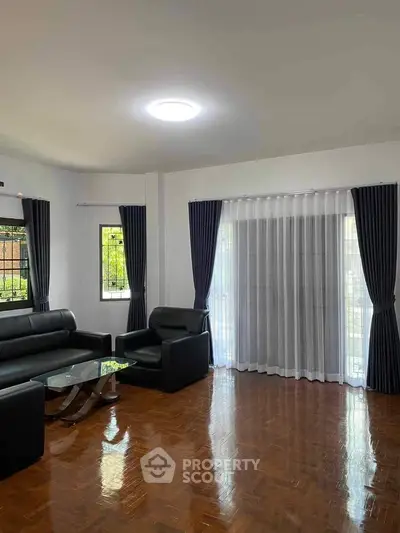 Spacious living room with modern black leather sofas and large windows with curtains.