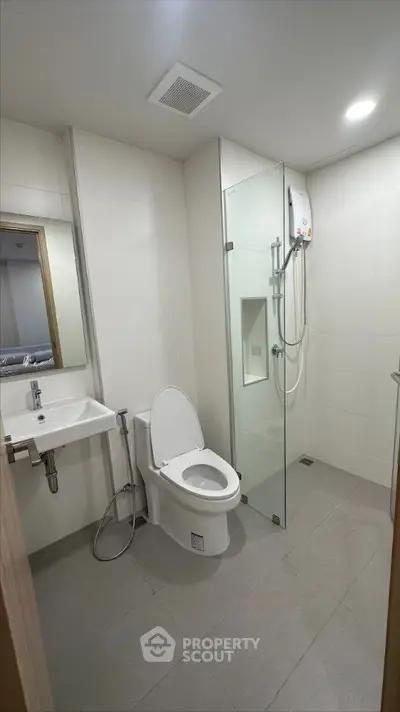 Sleek modern bathroom with glass shower enclosure, wall-mounted sink, and well-lit mirror, perfect for contemporary living spaces.
