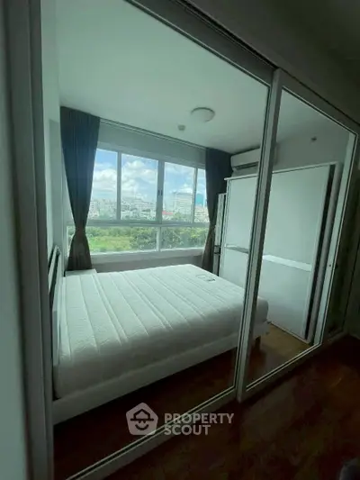 Modern bedroom with large window and mirrored closet doors, offering a bright and airy atmosphere.
