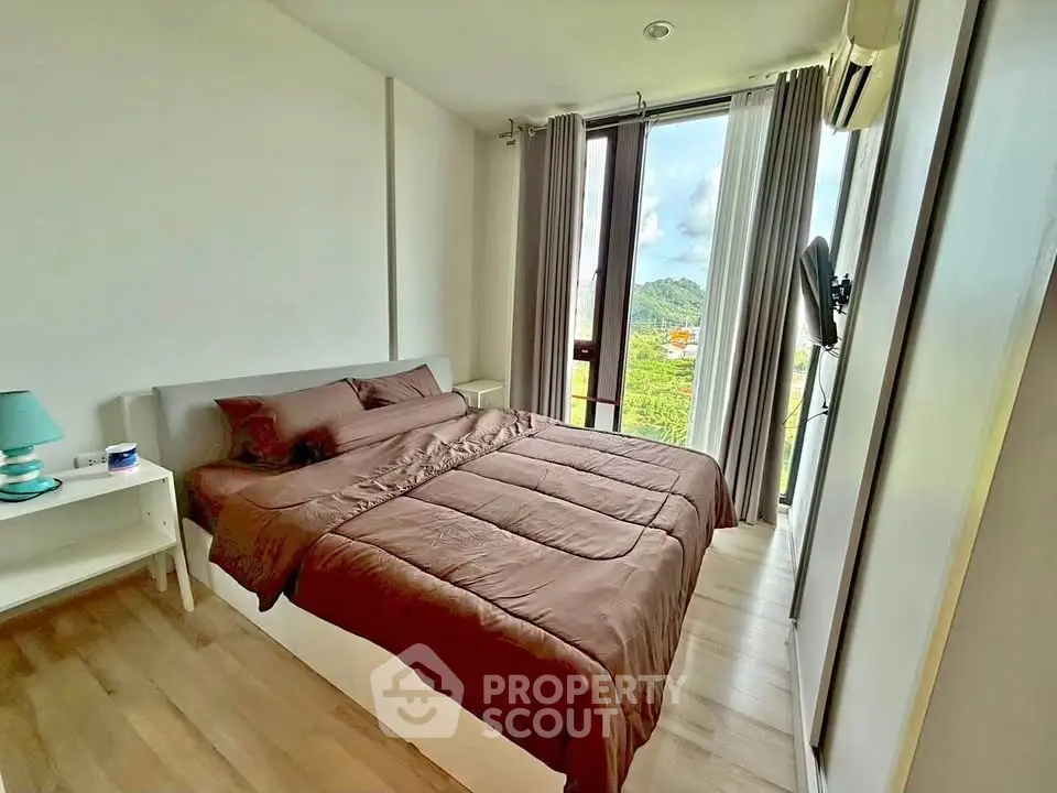 Cozy bedroom with large window offering scenic views, featuring a comfortable bed and modern decor.
