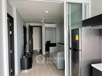Modern apartment interior with sleek kitchen and cozy living area, featuring a stainless steel fridge and stylish decor.