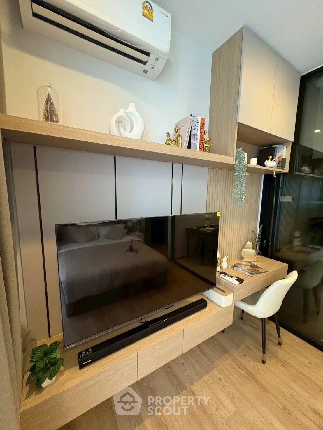 Modern living room with sleek TV setup and stylish decor, featuring a cozy workspace and air conditioning.