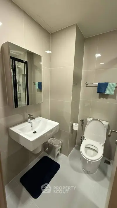 Modern bathroom with sleek fixtures and neutral tiles, featuring a spacious sink and toilet.