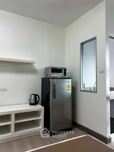 Compact kitchen corner with fridge, microwave, and kettle in modern apartment.