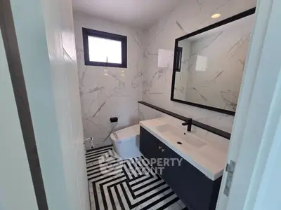 Modern bathroom with marble walls and geometric floor tiles, featuring a sleek vanity and large mirror.