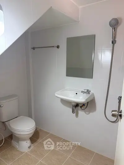 Modern bathroom with sleek fixtures and under-stair design, featuring a shower and compact sink.