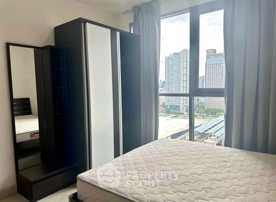 Modern bedroom with city view, featuring a large window, wardrobe, and bed frame in a high-rise apartment.