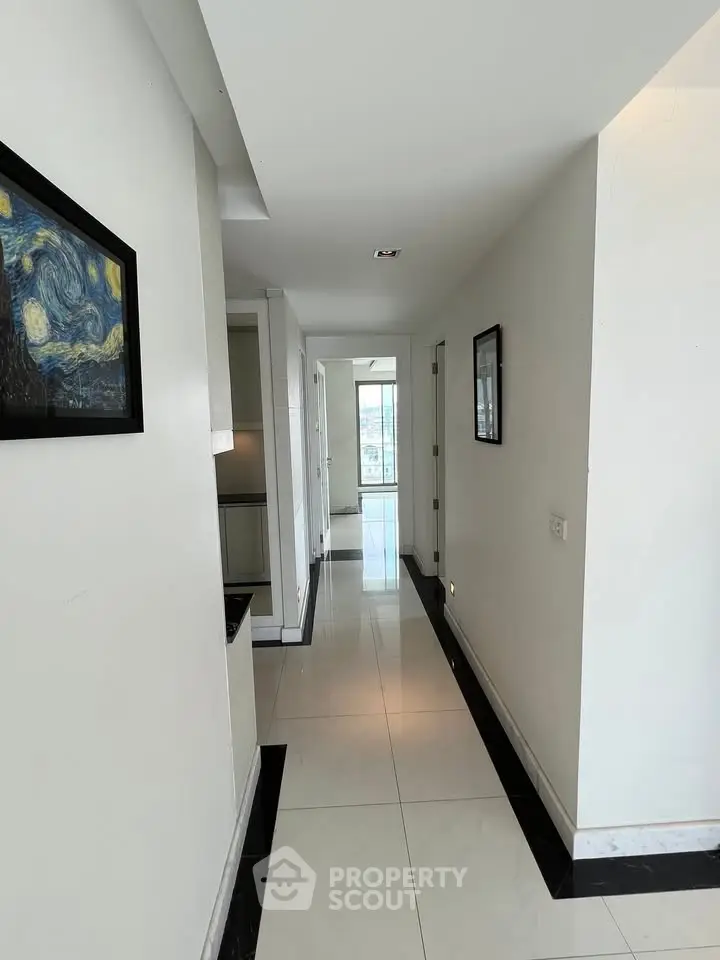 Sleek modern hallway with elegant tile flooring and framed artwork, leading to a bright window view.