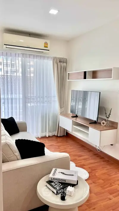Modern living room with stylish decor, large window, and mounted TV unit in a cozy apartment.