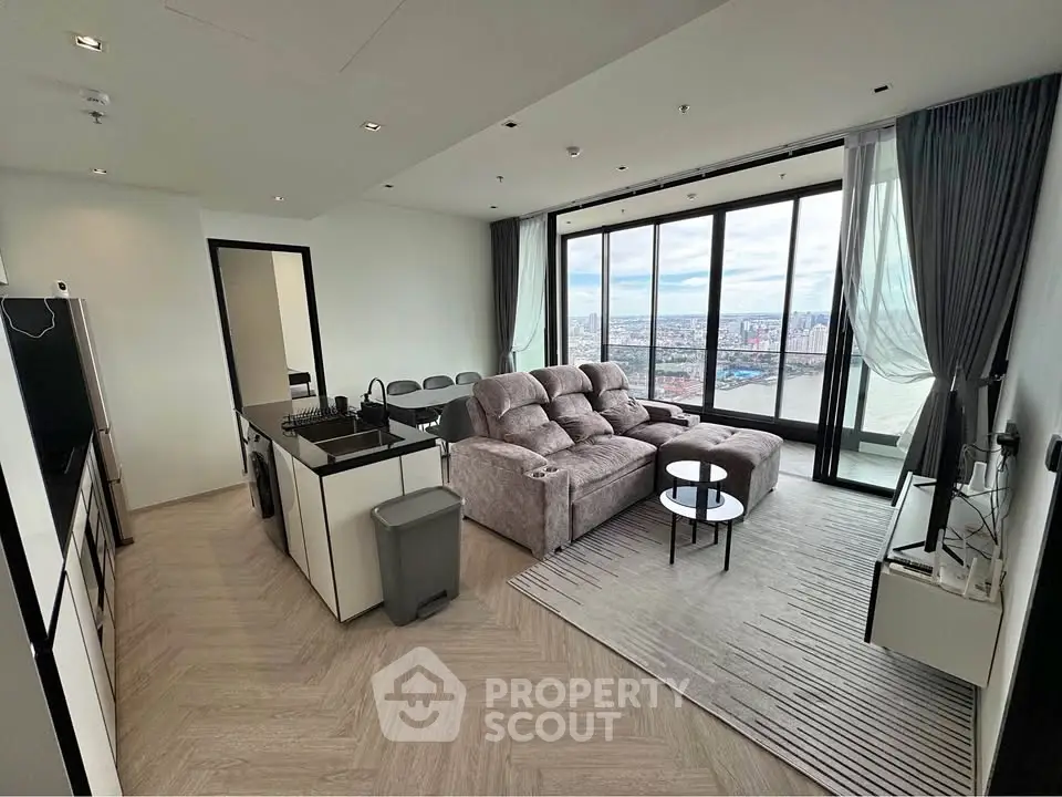 Modern living room with panoramic city view, cozy seating, and sleek kitchen area in open layout apartment.